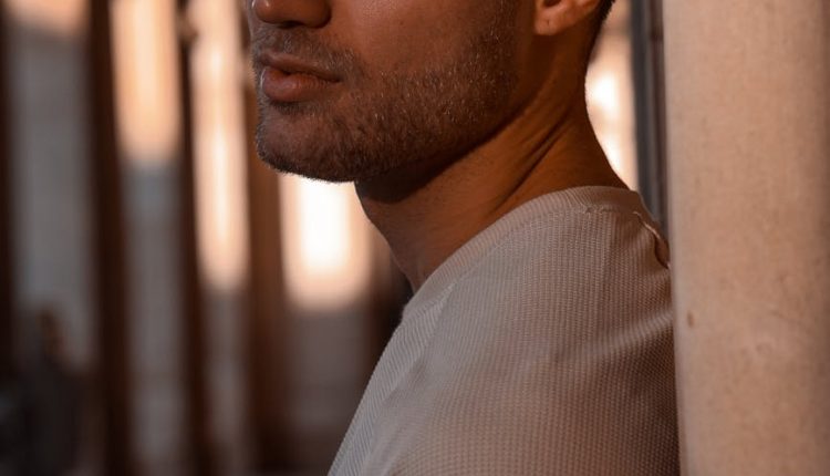 Portrait of a contemplative man leaning against a pillar, bathed in sunset light.
